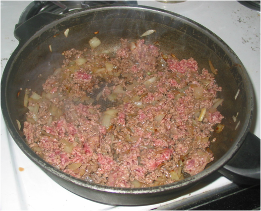 ground beef and onions in a skillet on the stove top frying