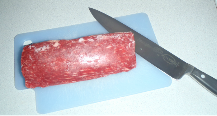 sligtly frozen beef tenderloin on a cutting board with a knife Picture