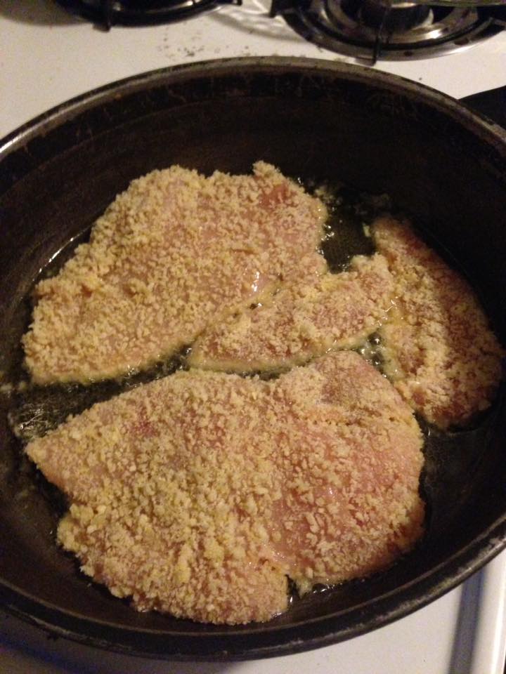 breaded chicken breast in frying pan before being flipped